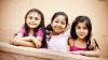 Three young girls sitting side by side smiling at the camera