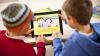 Two young boys playing a game on a tablet
