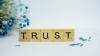 TRUST spelled out in wooden blocks with letters on, white background with blue flowers