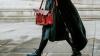 Person walking on concrete in a black coat carrying a red bag