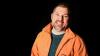 Man with very short hair, smiling, wearing orange coat.
