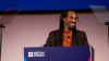 Benjamin Zephaniah smiling on stage, he is standing at a British Council branded podium, with a glass teleprompter on each side.