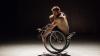 An atmospheric theatre scene of a dancer turning in his wheelchair under spotlight