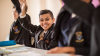 Male student in school uniform with hand raised