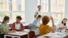 Five teenagers are interacting with a teacher in a classroom