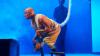 Actor on stage performing in a production of Confessions of a Shinagawa Monkey. The stage background is blue and the actor is wearing a long tail. Another actor can be seen in the background.