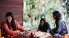 Three women sitting at a table, in conversation and laughing. On the table there are threads of different coloured cotton.
