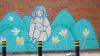A painted mural on a red brick wall: an young woman sits on a mountainous bright blue landscape with a bird perched on her knee. The image holds a sense of contemplation.