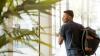 Young man wearing a backpack walking out of a glass door 