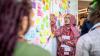Farhana Chowdhury points at a board of post-it notes, watched by two other people.