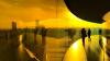 Young people looking out the window of a glass building, in the bright yellow glow of the sun setting.