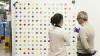 Two students in the foreground discuss a Damien Hirst spot painting in the background