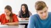 Three adults are sitting at desks completing assessments