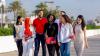 A group of young people walking along outside in sunny Dubai. Palm trees can be seen in the background.