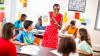 A teacher holds up a piece of paper, she is showing it to her class of young pupils.