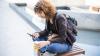 Young woman sitting cross-legged wearing a backpack and looking at her mobile phone