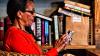 Woman seated beside book shelf and using mobile phone