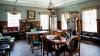 A library room decorated in a Victorian style with a table and chairs and a desk, plus bookcases against the walls.