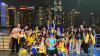 A group of school children celebrating their arrival in China, against a backdrop of skyscrapers lit up against the night sky.