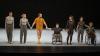 Seven mixed disabled and non-disabled dancers link hands as they prepare to take a bow on an almost empty stage following a performance of ‘Mixed Doubles’ by Grootens, Kalampaliki, Tortelli and Espinosa, created as part of ‘Europe Beyond Access’