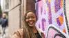 A young black woman standing against a colourful, graffiti-painted wall and smiling