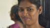 A woman smiling at the camera, another woman in the background wearing a sari.