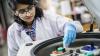 Female scientist in a lab coat performing an experiment, placing a test tube into a machine.