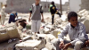 Young boy sitting among ruins with other people standing in the background