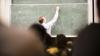 A lecturer writing on a blackboard in front of a class of students