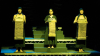 Three people on stage, holding long packages in front of themselves.
