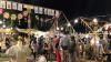 A busy market scene of colourful crafts, food vendors, and people browsing and buying goods.