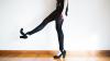 The legs of a woman wearing black tights and shoes with one leg raised in the air.
