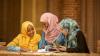 Three women sit together looking at a book.