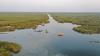 A view from above of the green marshes, with waterways running through, a boat and houses can also be seen.