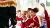 A school girl smiles up at her teacher. Other children can be seen in the background.