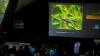 Crowd in front of a stage displaying a large screen with an image of an insect.