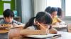 Two girls and a boy sat writing at their desks in a classroom