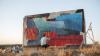 An artist paints a large rectangular canvas outdoors in nature