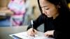 An adult is sitting at an exam desk writing on an exam paper