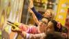 Two children pointing at a screen on a wall. Teacher is assisting them. 