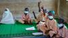 Children sitting on floor in a classroom with hands raised.