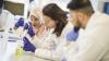 An image of three lab technicians wearing lab coats, goggles and gloves conducting a lab experiment.