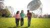 International students walk beside a giant radio telescope in animated conversation