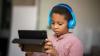 A young learner is sitting looking at a tablet with headphones on.