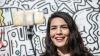 A young woman in front of a murales.