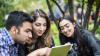 Three young adults in a park looking at an Ipad.