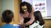 A female teacher leaning over a table looking at a resource with a young girl.