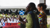 Two ladies, on Ghanaian and one Scottish address students at an outdoor assembly in Ghana